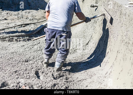 Travailleur de la construction piscine travaillant avec un Bullfloat sur béton humide Banque D'Images