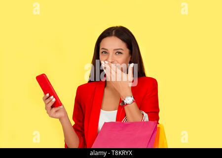 Portrait d'une femme assez excité avec des sacs colorés looking at mobile phone rire heureux fashion girl isolé sur fond jaune. Mul Banque D'Images
