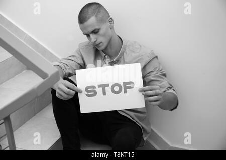 Teenage boy holding feuille de papier avec mention "STOP tout en étant assis sur des escaliers à l'école Banque D'Images