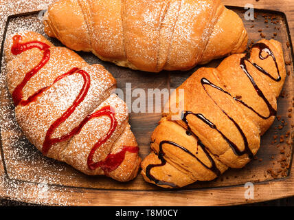 Délicieux croissants avec de la confiture et du sirop de chocolat sur planche de bois Banque D'Images