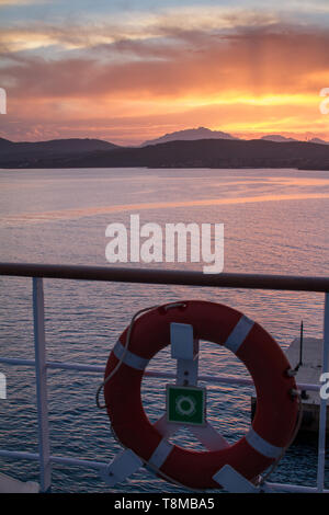 Lever du soleil sur la mer de Sardaigne côte avec la couleur orange intense vu de la mer sur le ferry qui est sur le point d'accoster avec bouée dans l'avant-plan Banque D'Images