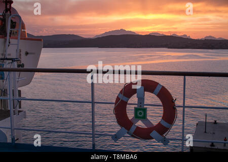 Lever du soleil sur la mer de Sardaigne côte avec la couleur orange intense vu de la mer sur le ferry qui est sur le point d'accoster avec bouée dans l'avant-plan Banque D'Images