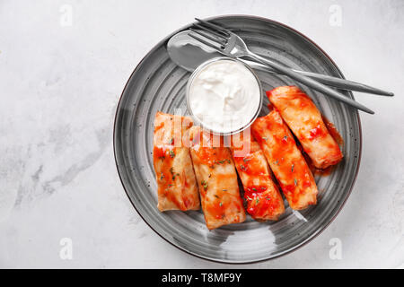 La plaque avec les feuilles de chou farcies à la sauce tomate et le bol de crème sure sur table lumineuse Banque D'Images