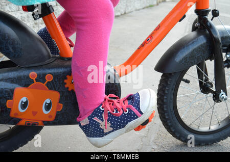 Détail d'une petite fille portant un pantalon rose et bleu chaussures en pointillés, les pieds sur les pédales, apprendre à conduire un vélo pour les enfants Banque D'Images