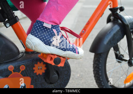 Détail d'une petite fille portant un pantalon rose et bleu chaussures en pointillés, les pieds sur les pédales, apprendre à conduire un vélo pour les enfants Banque D'Images