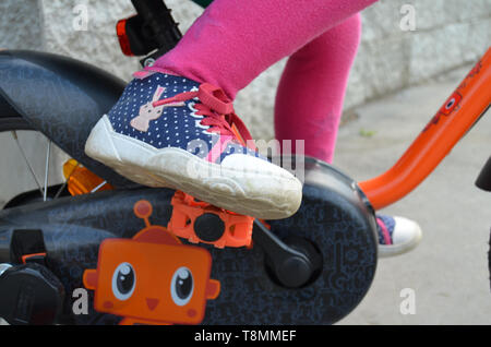 Détail d'une petite fille portant un pantalon rose et bleu chaussures en pointillés, les pieds sur les pédales, apprendre à conduire un vélo pour les enfants Banque D'Images