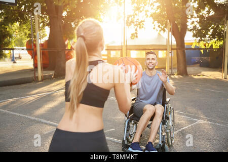 Jeune homme en fauteuil roulant et la formation sportive woman with ball en extérieur Banque D'Images