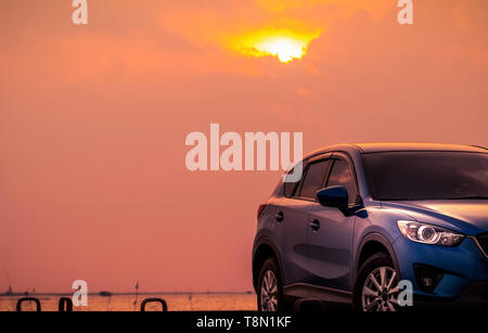 Vus compact bleu sport voiture avec un design moderne et stationné sur la route en béton par la mer au coucher du soleil le soir. Technologie voiture hybrides et électriques conc Banque D'Images