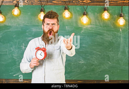 Régime de l'annexe et concept. Enseignant dans les lunettes est titulaire d'un réveil. Homme à barbe à crier face à argumenter l'expression. Hipster barbu est titulaire d'réveil, tableau sur toile de fond, l'espace de copie. Banque D'Images