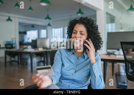 Smiling businesswoman ordering quelque chose en utilisant son portable et une carte de crédit Banque D'Images