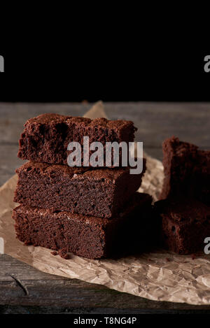 Pile de petits morceaux carrés de chocolat Gâteau Brownie Brown sur le papier parchemin, fond noir Banque D'Images