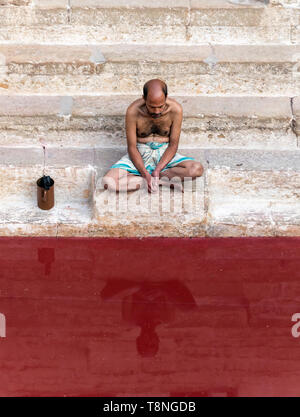 L'homme prie dans le Manikarnika bien avec de l'eau teintée de rouge, Varanasi, Inde Banque D'Images