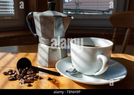 Pot de café moka en aluminium blanc, tasse de café noir, avec soucoupe et cuillère en argent et les grains de café sur une table de cuisine Banque D'Images