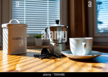 Tin café blanc avec grains de café, cafetière moka aluminium blanc, tasse de café noir, avec soucoupe et cuillère en argent et les grains de café sur la table de cuisine Banque D'Images