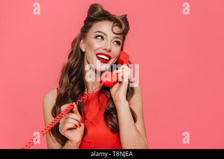 Portrait d'une jeune et belle pin-up girl wearing dress isolés sur fond rose, conversation au téléphone fixe Banque D'Images