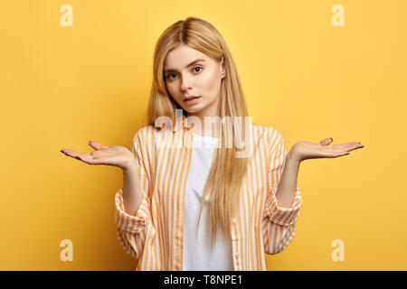 Femme a déplu à expression, porte chemise rayée,T-shirt blanc, pose contre studio jaune background.femme n'est pas sûr de son choix. fille ne sait pas quoi faire dans cette situation Banque D'Images