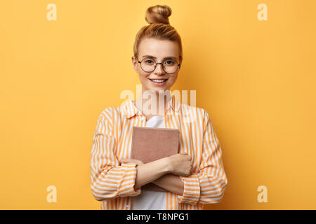 Belle blonde avec des élèves un livre dans ses mains à la recherche de l'appareil photo. la photo en gros.La connaissance est puissance. Banque D'Images