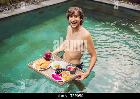 Plateau de petit-déjeuner dans la piscine, petit-déjeuner en hôtel de luxe flottant. L'homme se détendre dans la piscine de boire et manger des smoothies de fruits smoothie, bol Banque D'Images