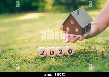 Concept pour l'achat d'une maison en l'an 2020. Une main tient une maison modèle au-dessus d'une prairie. Formulaire dés le mot "2020". Banque D'Images