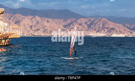 Planche à voile d'un enfant dans le port d'Eilat en Israël avec le port d'Akaba en Jordanie dans l'arrière-plan Banque D'Images