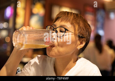 Taiwanais mature femme d'origine chinoise de boire une bière dans un cadre chaleureux, agréable restaurant Banque D'Images