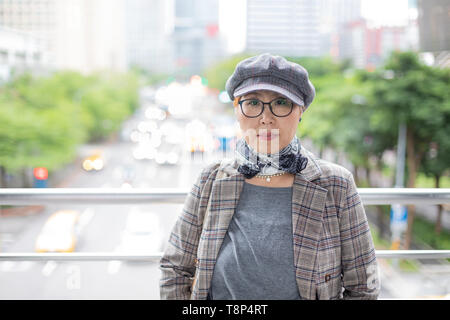 Taiwanais à la mode femme d'origine chinoise appuyé contre balustrade avec ville en arrière-plan Banque D'Images