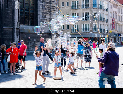 Homme faisant des bulles et des enfants essayant de les attraper souriant et riant en profitant du divertissement gratuit,Gand,Belgique,Europe. Banque D'Images