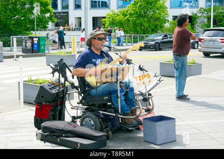 Un musicien de rue dans un fauteuil roulant avec ampli guitare jaune et joue pour les passants dans une rue. Vancouver, B. C., Canada Banque D'Images