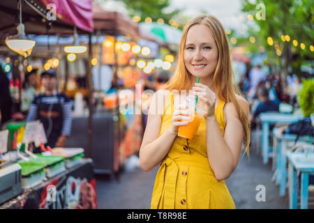 Woman drinking orange juice sur le marché asiatique Banque D'Images