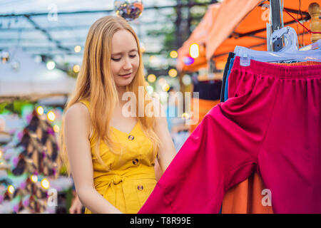 Vente, vente au détail, les magasins et les vêtements concept - Femme choisit les vêtements dans le marché asiatique Banque D'Images