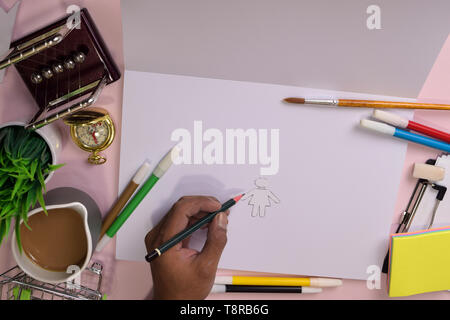 Vue du dessus de la main de l'homme dessin sur une table rose, la préparation pour faire ses devoirs dans un ordinateur portable avec un marqueur à la main. Dimensions Bureau Concept. Banque D'Images