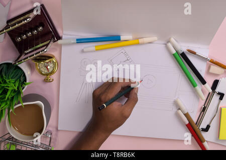 Vue du dessus de la main de l'homme dessin sur une table rose, la préparation pour faire ses devoirs dans un ordinateur portable avec un marqueur à la main. Dimensions Bureau Concept. Banque D'Images