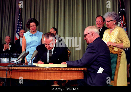 Le Président Lyndon B. Johnson signe la loi d'assurance-maladie à la Harry S. Truman Library à Independence, Missouri. L'ancien président Harry S. Truman est assis à la table avec le président Johnson. Les éléments suivants sont à l'arrière-plan (de gauche à droite) : Le sénateur Edward C. Long, un homme non identifié, Lady Bird Johnson, le sénateur Mike Mansfield, Vice-Président Hubert Humphrey, et Bess Truman. Juillet 30,1965 Banque D'Images