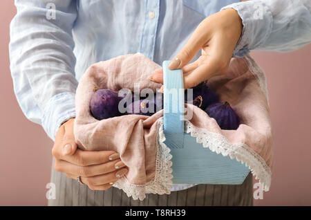 Femme tenant un panier de figues mûres fraîches sur un fond de couleur, gros plan Banque D'Images