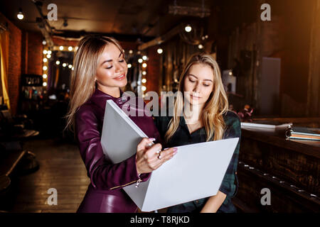 Salon de beauté, cheveux Colorant et personnes concept. Smiling blonde jeune femme et coiffure choisir la couleur de cheveux de coloration de cheveux dans la palette avant de salo Banque D'Images