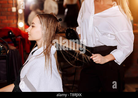 Coiffeur professionnel à l'aide d'un sèche-cheveux tandis que sa coiffure female client . Belle jeune femme obtenir une nouvelle coupe de cheveux au salon de beauté. Banque D'Images