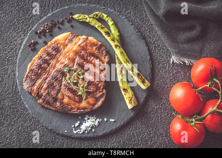 Pavé de boeuf grillé garni d'asperges et tomates fraîches sur le conseil de pierre noire Banque D'Images