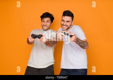 Deux amis à jouer aux jeux vidéo sur fond orange Banque D'Images