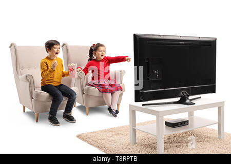 Heureux petit garçon et fille assise dans un fauteuil à regarder la télévision et eating popcorn isolé sur fond blanc Banque D'Images