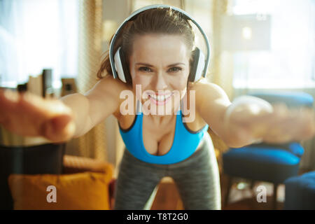 Happy active femme dans les écouteurs en vêtements de sport dans le salon moderne d'étirement. Banque D'Images