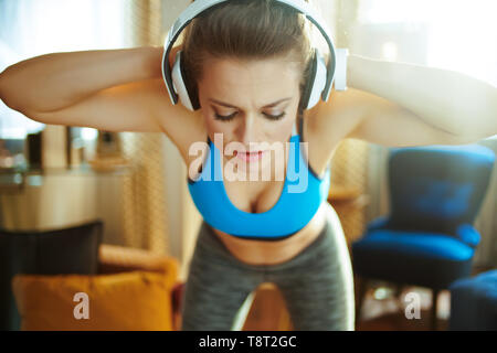 Femme active dans les écouteurs en vêtements de sport dans la maison moderne d'étirement. Banque D'Images