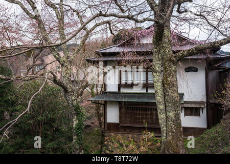 Bâtiment traditionnel japonais sur colline boisée avec des fleurs de cerisier début d'ouvrir au début du printemps Banque D'Images