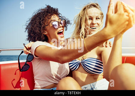 Deux jeunes femmes amis assis ensemble sur un bateau qui autoportraits ensemble et rire pendant leurs vacances d'été Banque D'Images