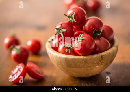 Tomates cerises fraîches dans bol en bois sur table en bois Banque D'Images