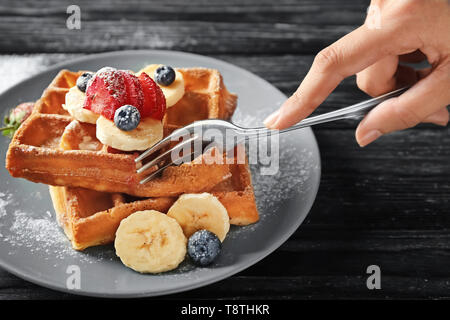 Femme manger de délicieux gaufres et fruits rouges sur fond de bois Banque D'Images