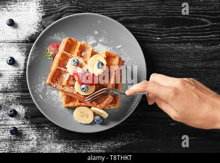 Femme manger de délicieux gaufres et fruits rouges sur fond de bois Banque D'Images