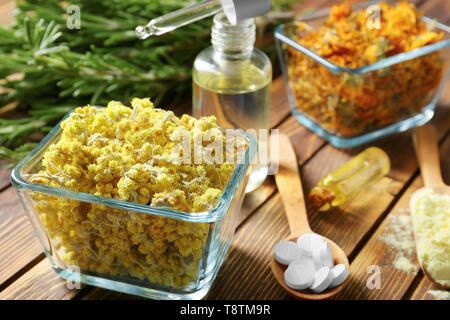 Boules de fleurs, bouteilles d'huile essentielle et des pilules sur table en bois Banque D'Images