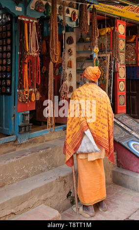 Hindu sadhu (saint homme) à l'extérieur de magasin qui vend des perles et autres objets artisanaux en marché près de Durbar Square, Patan, Vallée de Katmandou, Népal Banque D'Images