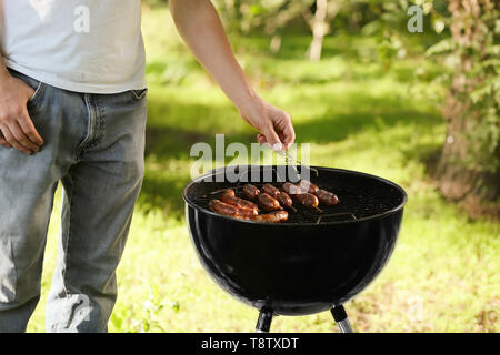 Man cooking sausages sur la grille du barbecue en plein air Banque D'Images