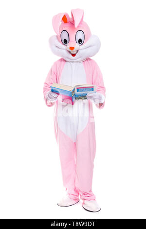 Taille de la vie avec costume de lapin livre sur fond blanc. Lapin de Pâques lit le livre, reçoit une éducation, essayant d'être intelligent Banque D'Images